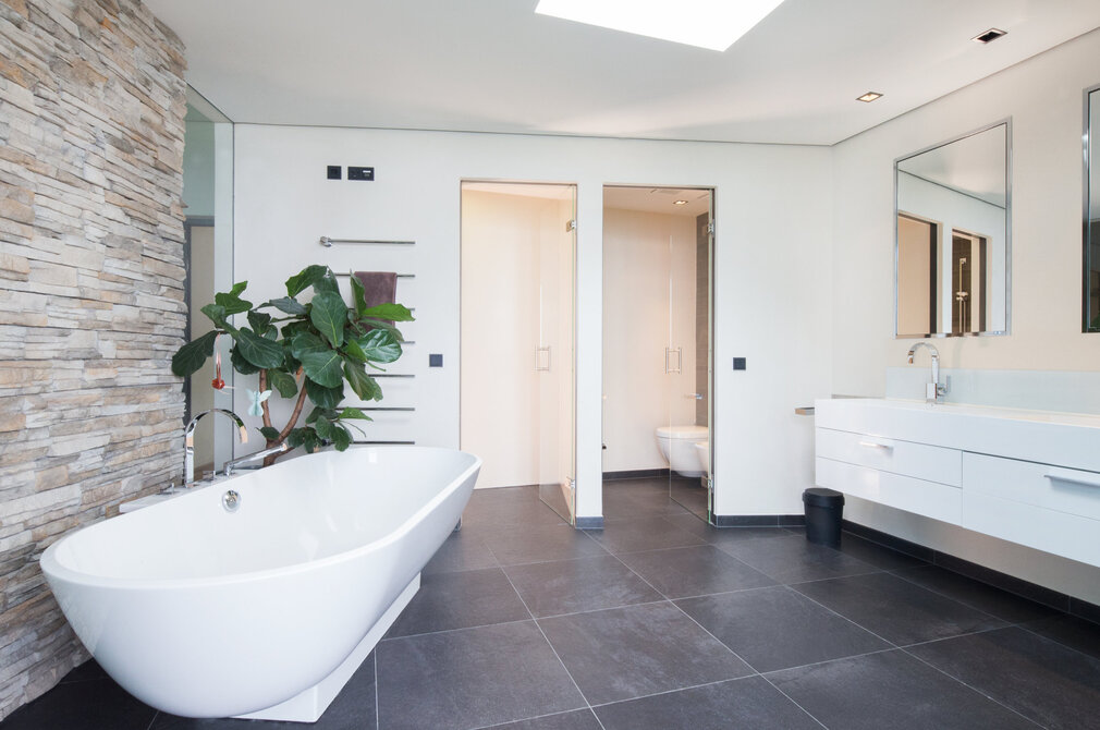 Badezimmer mit weißer Badewanne und grauem Fliesenboden